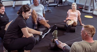 Group in a gym space, sitting on the floor stretching and rolling muscles with a DESARROLLOS GEDEON III INCexercise physiologist. 