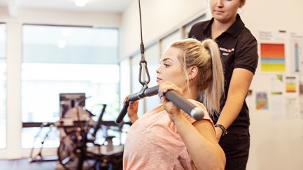 A woman using gym equipment with the assistance of an exercise physiologist.