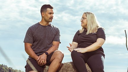 A Mates4Mates staff member and client sitting together on a rock talking.