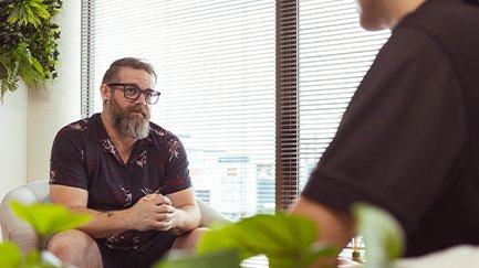 A client leaning forward in their chair, talking with a Mates4Mates psychologist in their private session.