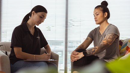 Client sitting in an appointment with a Mates4Mates social worker who is writing notes. 