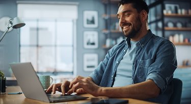 Person sitting in front of a laptop while sitting at a desk, typing and smiling. 