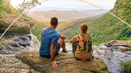 Two people outdoors looking over a waterfall on a clear blue day. 