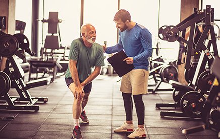 Older man and an exercise physiologist working through an exercise in a gym setting. 