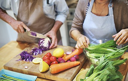 Two people in a kitchen setting, preparing and cutting vegetables on a chopping board. 