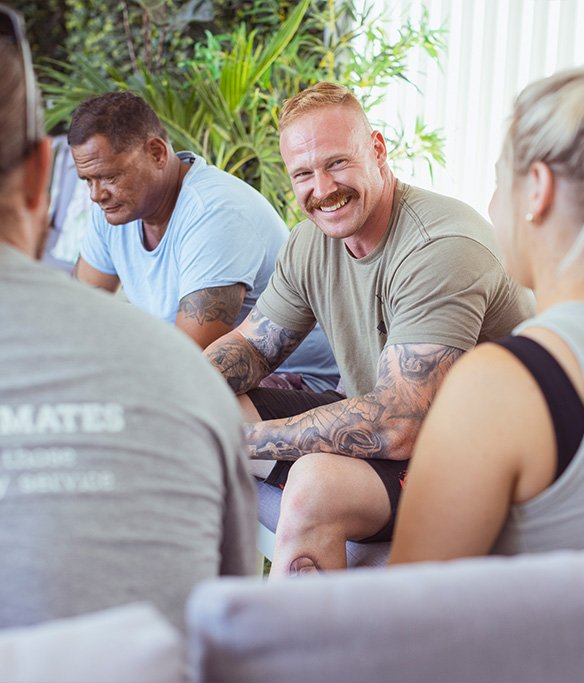 Group sitting together having a coffee and a chat, one person is smiling at the camera. 