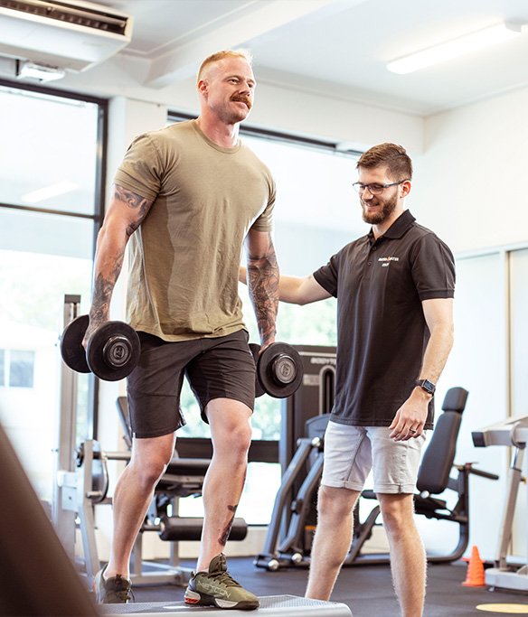 A person in a exercise physiology session with a staff member guiding them through a weighted step up exercise. 