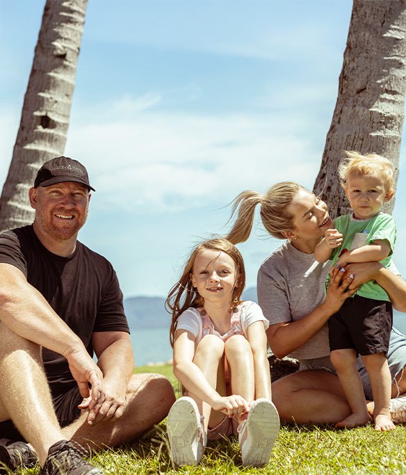Family of four sitting together outside under palm trees